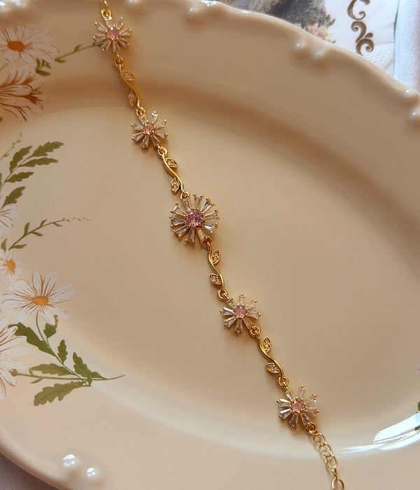 Pembe zirkon ve baget taşlı çiçek gold bileklik dekoratif tabak üzerinde