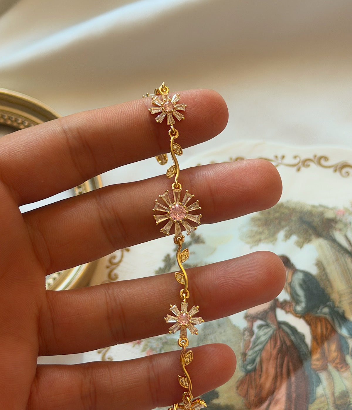 Pembe merkezli baget zirkon taşlı çiçek gold bileklik elde yakın çekim