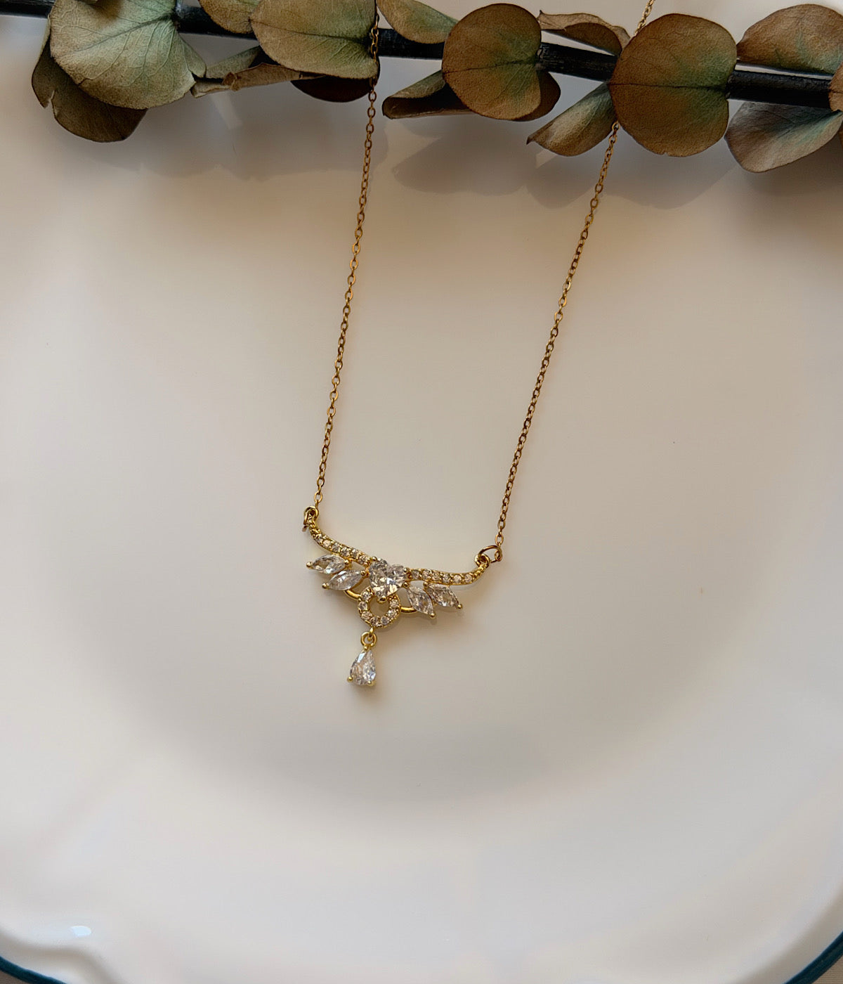 Kanat ve damla detaylı zirkon taşlı gold kolye dekoratif tabak üzerinde