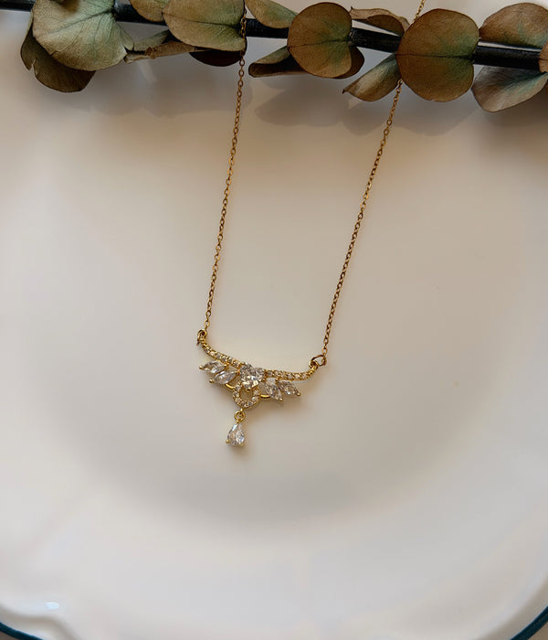 Kanat ve damla detaylı zirkon taşlı gold kolye dekoratif tabak üzerinde
