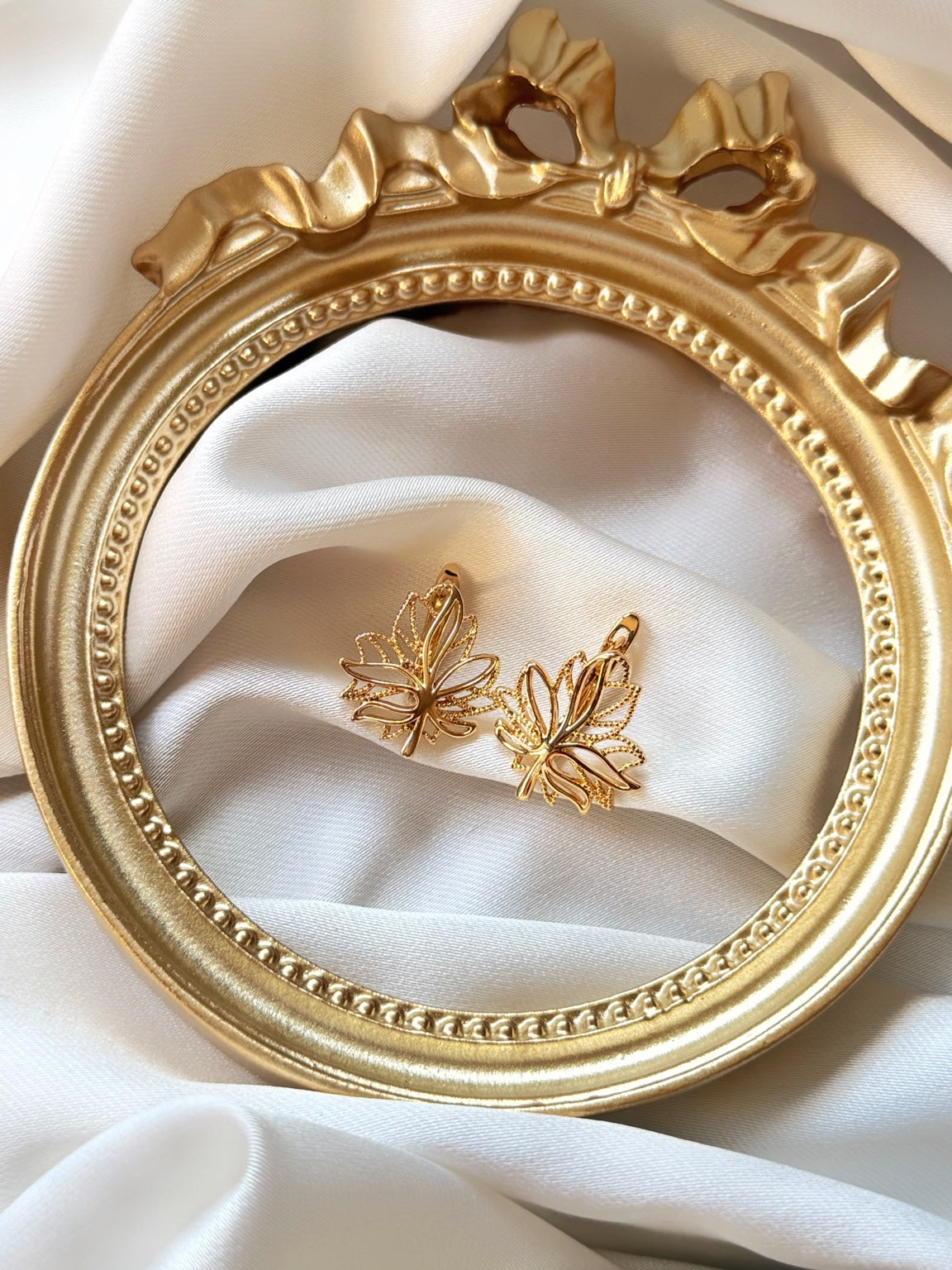 Yaprak figürlü gold kadın küpe çiftinin dekoratif çerçeve içinde görünümü