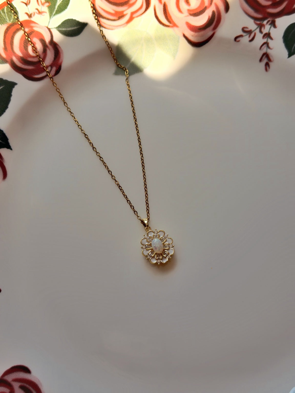 Gül desenli porselen üzerinde ince gold zincirli beyaz çiçek kolyenin genel görünümü