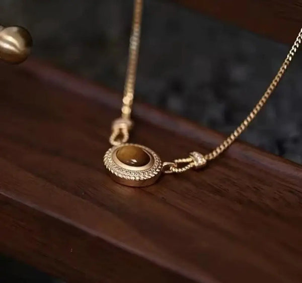 Saatli kadın takı setindeki yuvarlak kahverengi taşlı ve şeffaf taş çevreli gold kolye