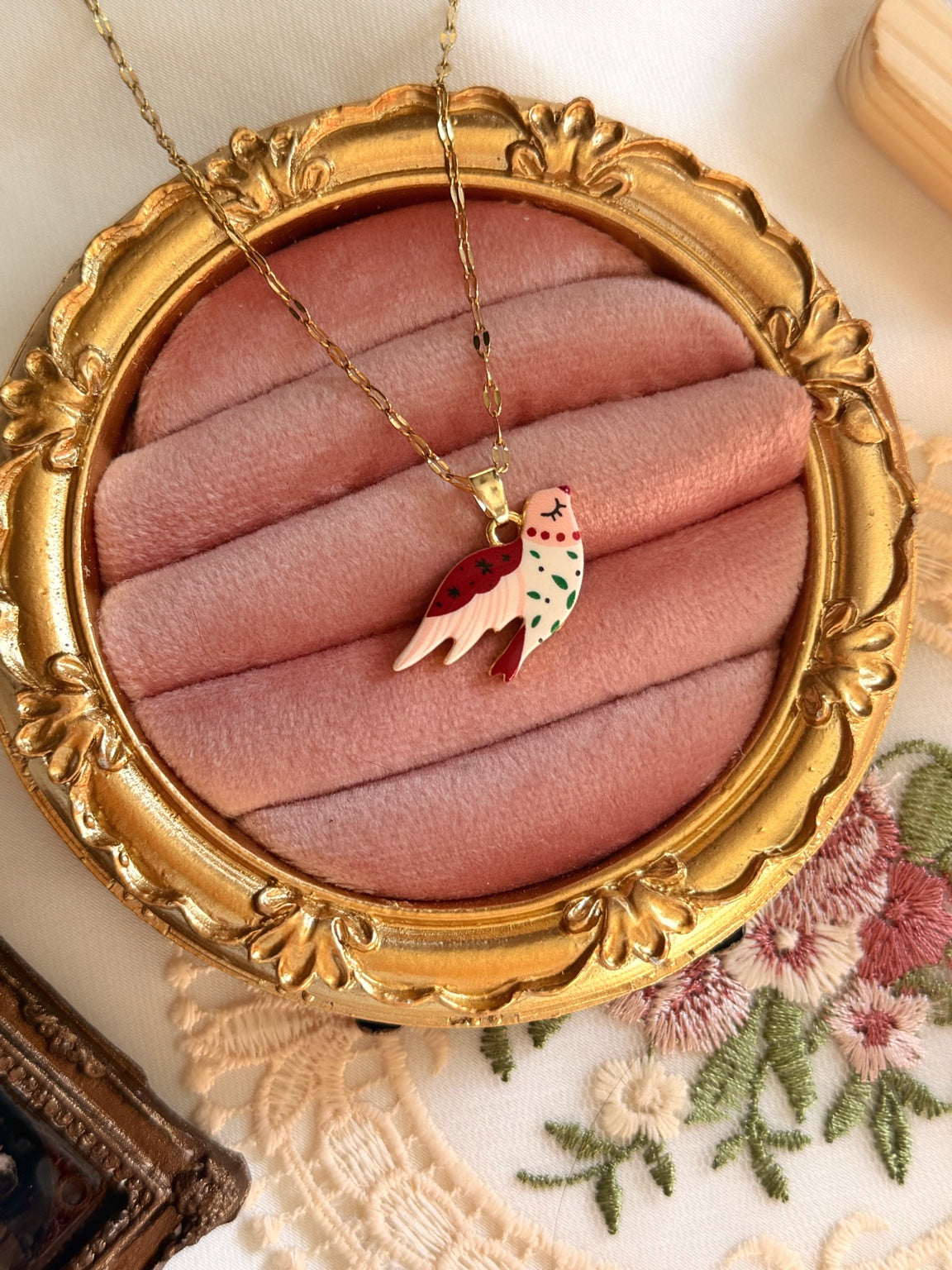 Pembe kadife çerçeve üzerinde kırmızı beyaz mineli kuş kolye ucu ve gold tonlu paslanmaz çelik zincir.
