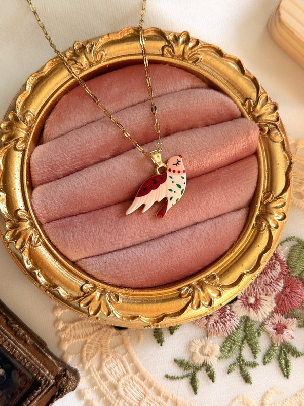 Pembe kadife çerçeve üzerinde kırmızı beyaz mineli kuş kolye ucu ve gold tonlu paslanmaz çelik zincir.