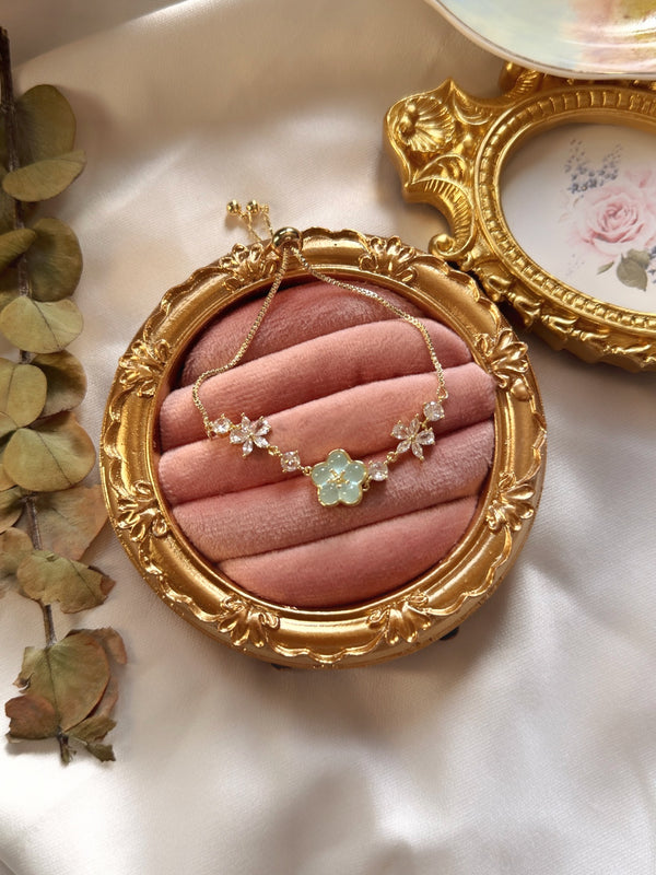 Mint yeşili çiçekli gold bilekliğin pembe kadife üzerinde zinciriyle birlikte görünümü
