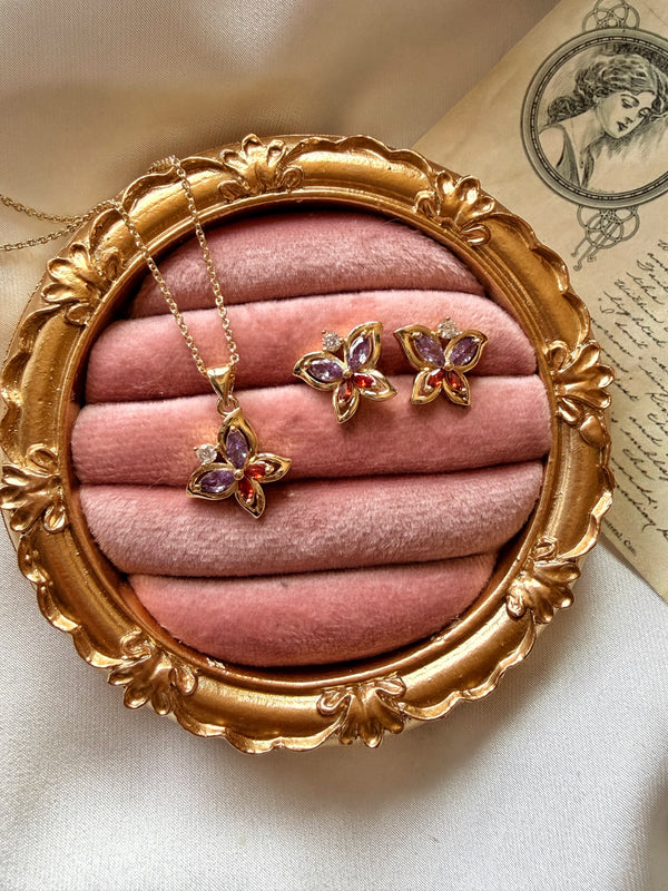 Mor ve kırmızı kelebek motifli kolye ve küpelerin pembe kadife üzerinde görünümü