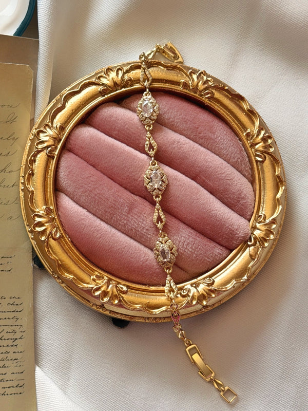 Gold çerçeveli pembe kadife üzerinde dikey duran oval taşlı bileklik ve klipsli uçları