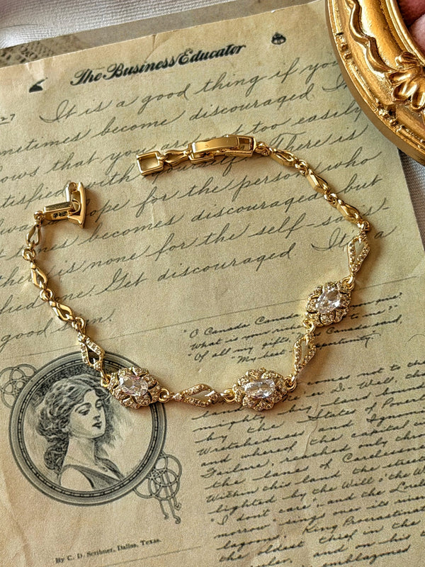 Yazılı kâğıt üzerinde oval taşlı çiçekli gold bilekliğin açık klipsi ve tüm zincir görünümü
