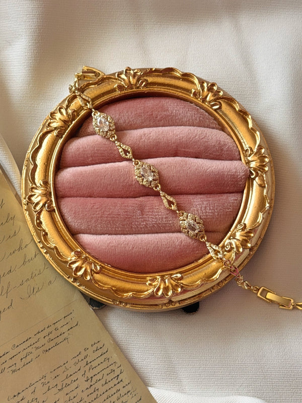 Yuvarlak pembe kadife takı standında çapraz sergilenen çiçek motifli gold bilekliğin genel görünümü
