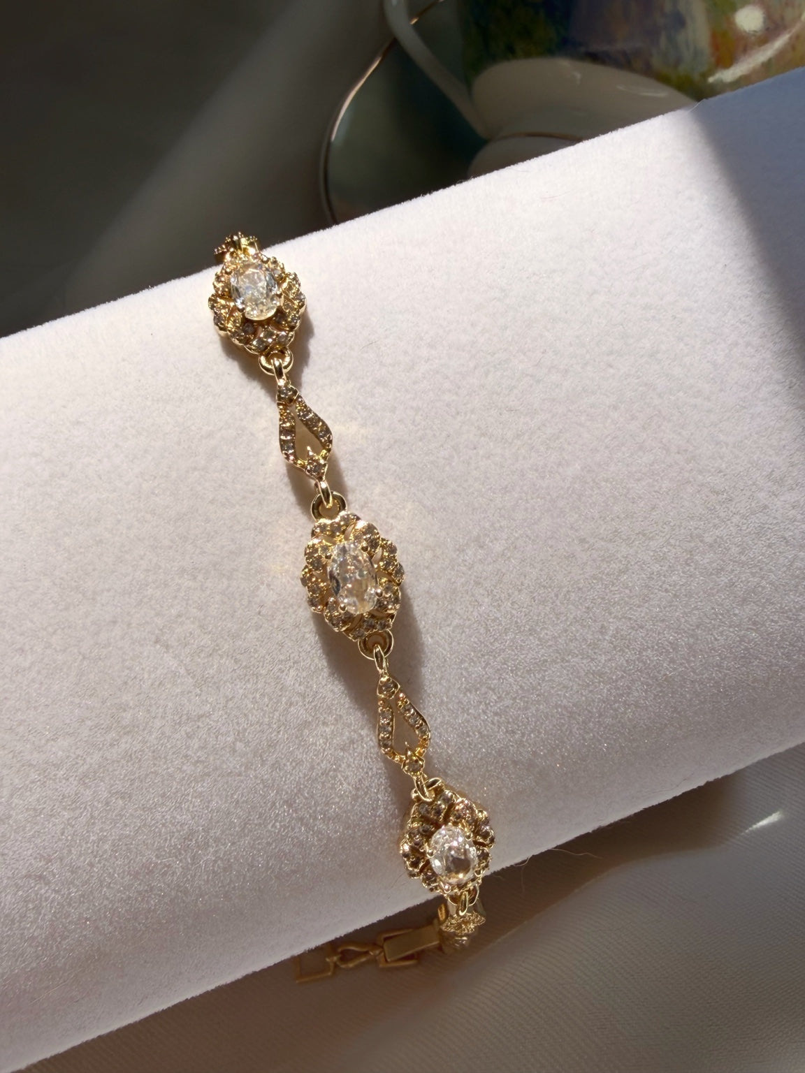 Beyaz bileklik standında üç çiçek motifli gold bilekliğin oval taş ve küçük taş ayrıntıları