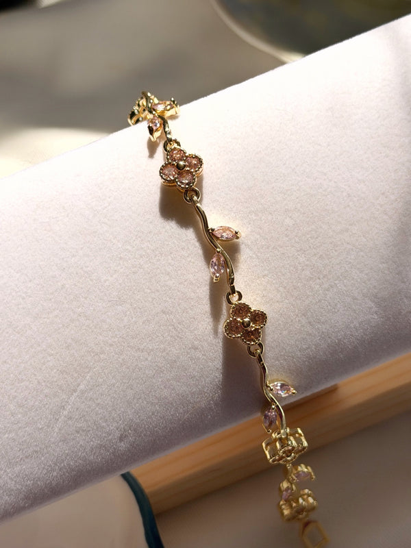 Pembe çiçek motifli bilekliğin kıvrımlı gold dal bağlantıları ve yaprak taşları