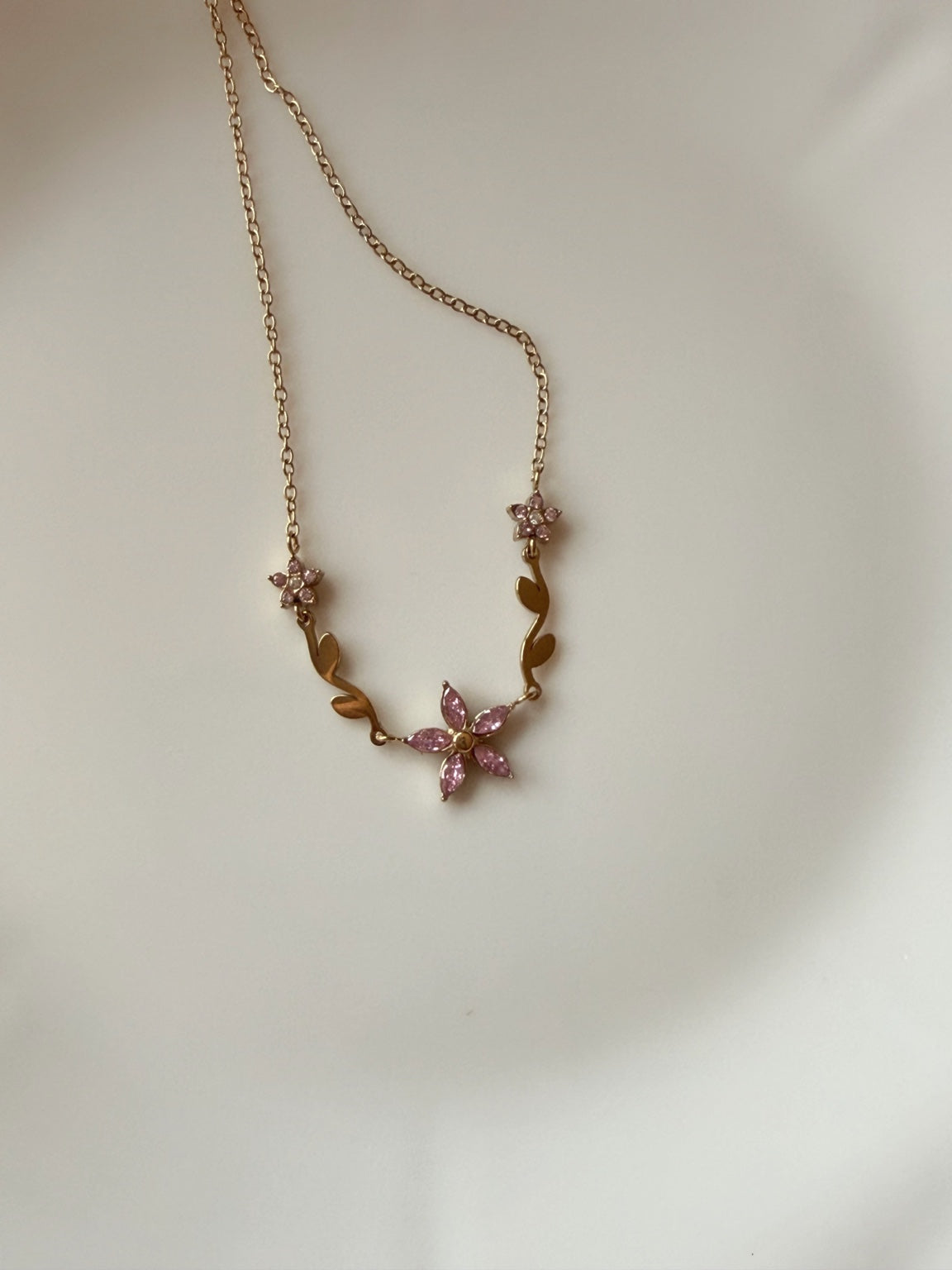 Pembe çiçekli ayarlanabilir gold çelik kolyenin düz zeminde görünümü