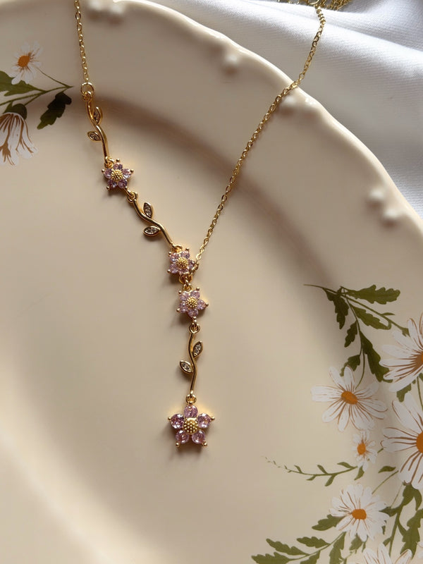 Pembe çiçekli dal detaylı gold Y kolyenin çiçek desenli tabak üzerinde görünümü
