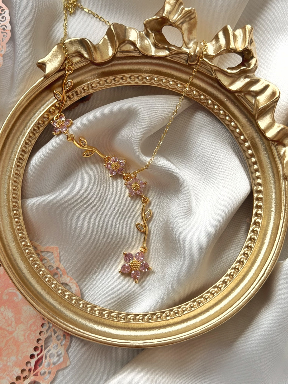 Pembe çiçekli dal detaylı gold kadın Y kolyenin saten ve gold çerçeve üzerinde görünümü