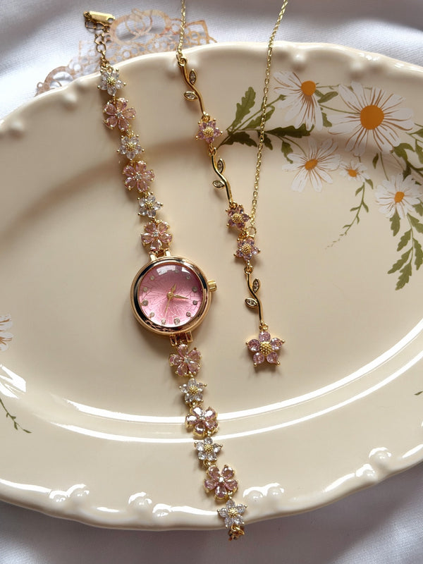 Pembe kadranlı çiçekli gold kadın saat ve Y kolye takı setinin çiçek desenli tabak üzerinde görünümü