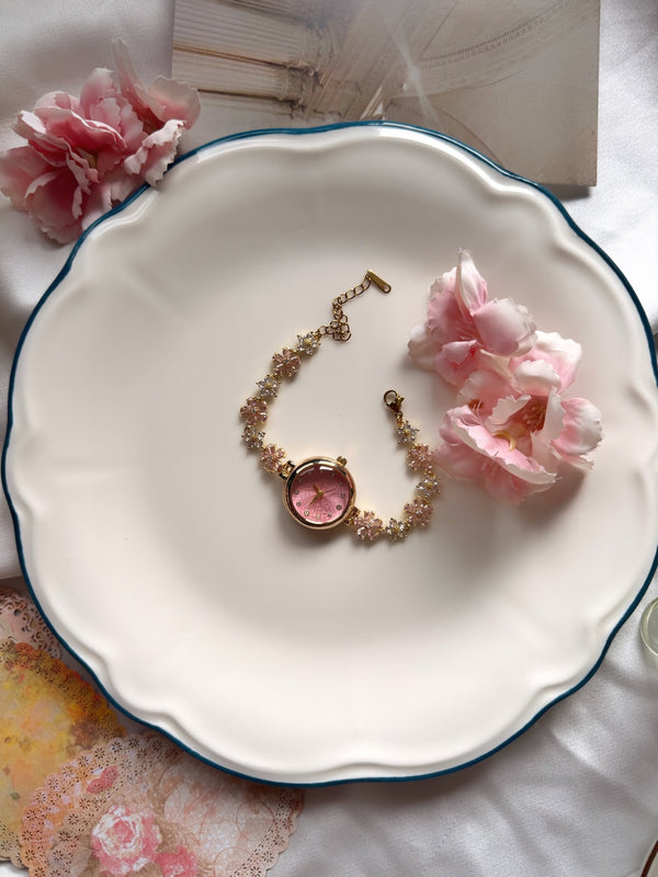 Pembe kadranlı çiçekli gold kadın saatin çiçek desenli tabakta tam ürün görünümü