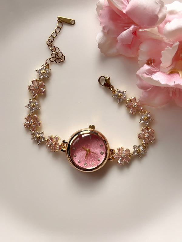 Pembe kadranlı çiçekli gold kadın saatin çiçeklerle dekoratif düz zeminde görünümü