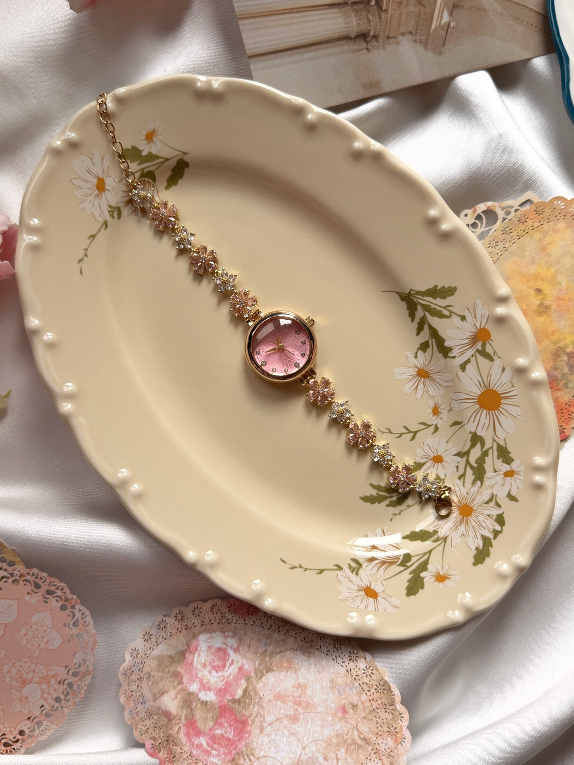 Pembe kadranlı çiçekli gold kadın saatin papatya desenli tabak üzerinde görünümü