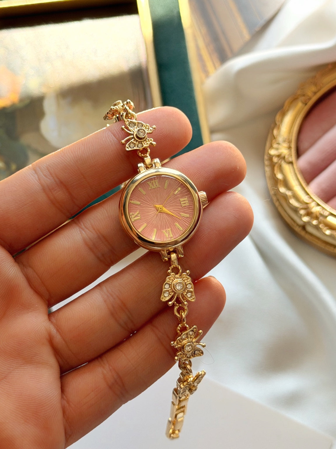Pembe kadranlı hareketli kelebek detaylı gold kadın saatin elde yakın görünümü