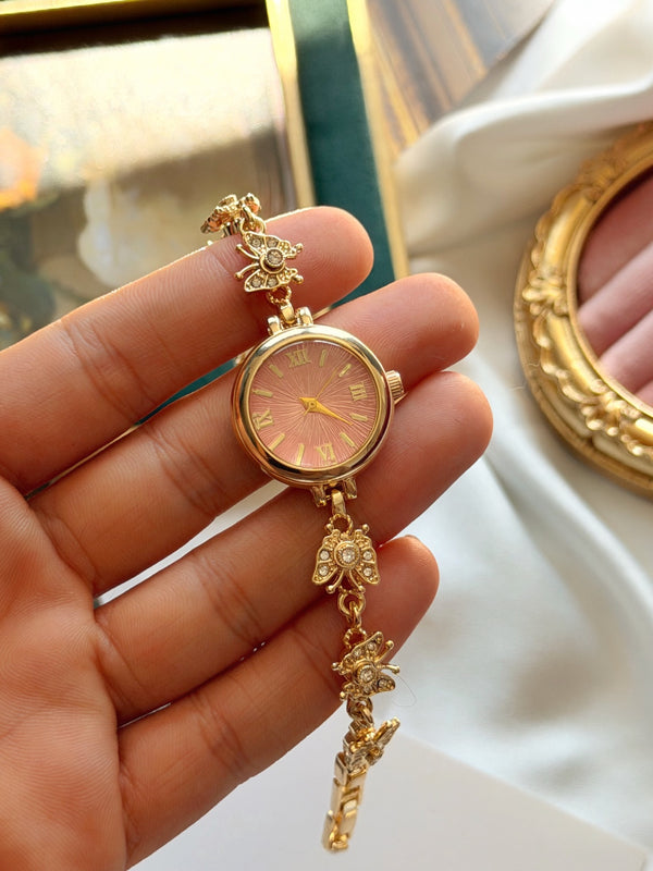 Pembe kadranlı hareketli kelebek detaylı gold kadın saatin elde yakın görünümü