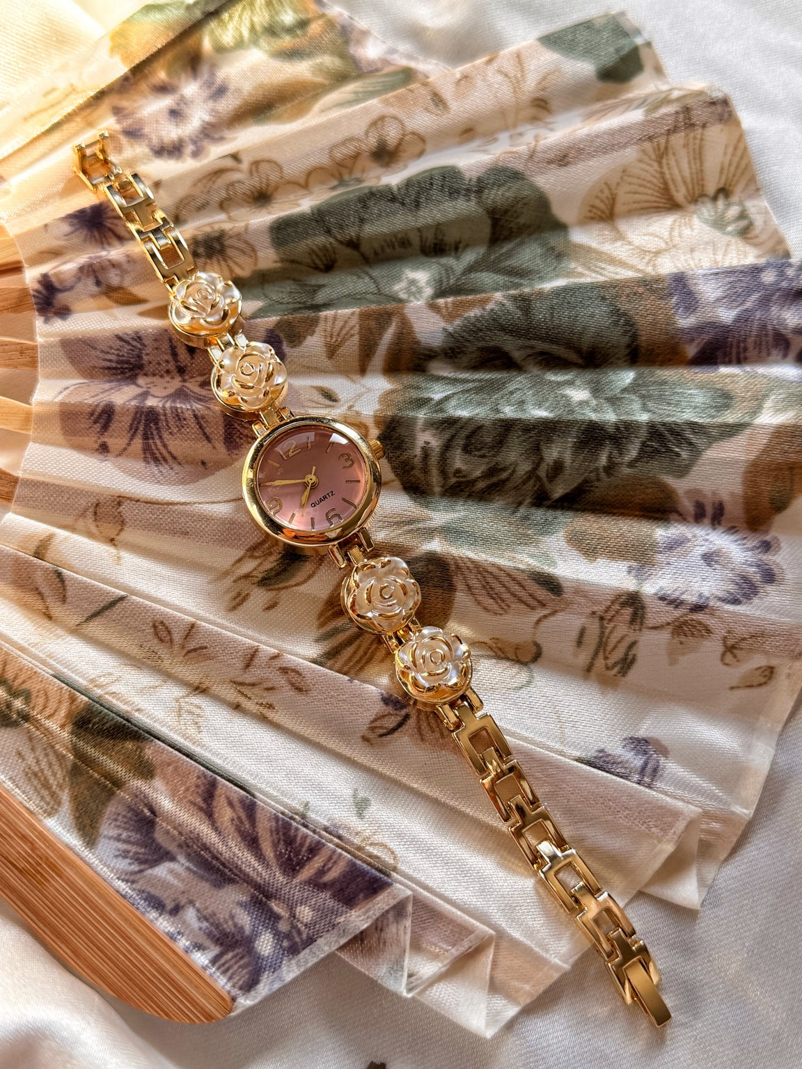 Pembe kadranlı beyaz gül motifli gold kadın saat ve metal kordon görünümü