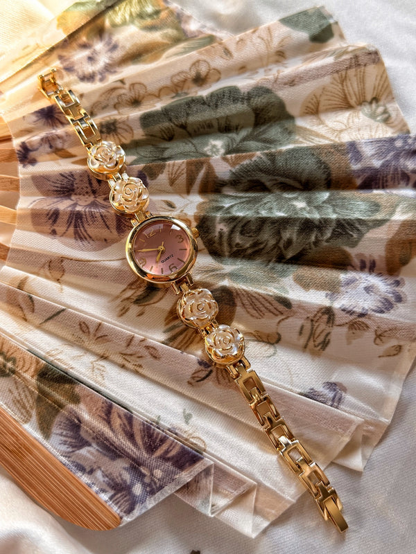 Pembe kadranlı beyaz gül motifli gold kadın saat ve metal kordon görünümü