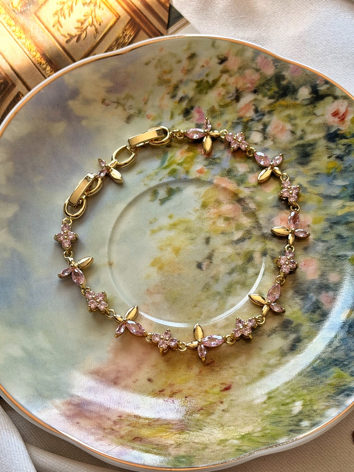 Pembe taşlı çiçek dalı gold kadın bilekliğin çiçekli porselen üzerinde görünümü