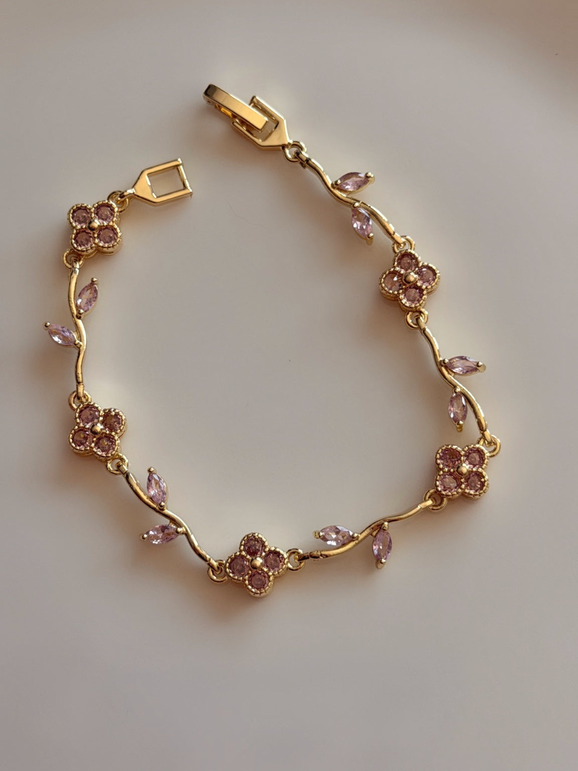 Pembe taşlı çiçek ve yaprak detaylı gold kadın bileklik, açık kilidiyle açık renk zeminde tam görünüm
