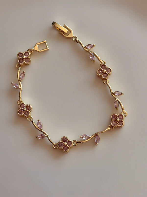 Pembe taşlı çiçek ve yaprak detaylı gold kadın bileklik, açık kilidiyle açık renk zeminde tam görünüm