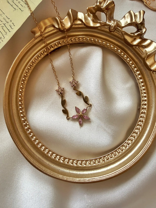 Pembe taşlı çiçek motifli gold kadın çelik kolyenin saten üzerinde tam görünümü