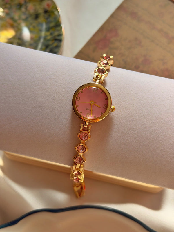 Pembe yuvarlak kadranlı gold bileklik saat, pembe taşlı geometrik bağlantıların yakın çekimi