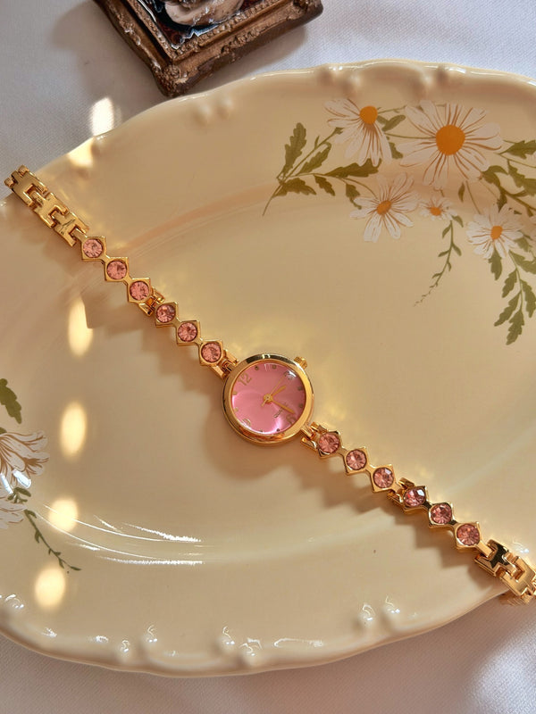 Çiçek desenli tabakta pembe yuvarlak kadranlı ve pembe taşlı gold metal kadın bileklik saat