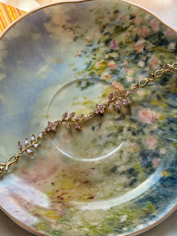 Pembe taşlı sarmaşık dal gold kadın bilekliğin çiçekli porselen üzerinde görünümü
