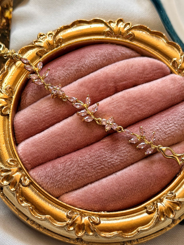 Pembe taşlı sarmaşık motifli gold kadın bilekliğin pembe kadife üzerinde yakın görünümü