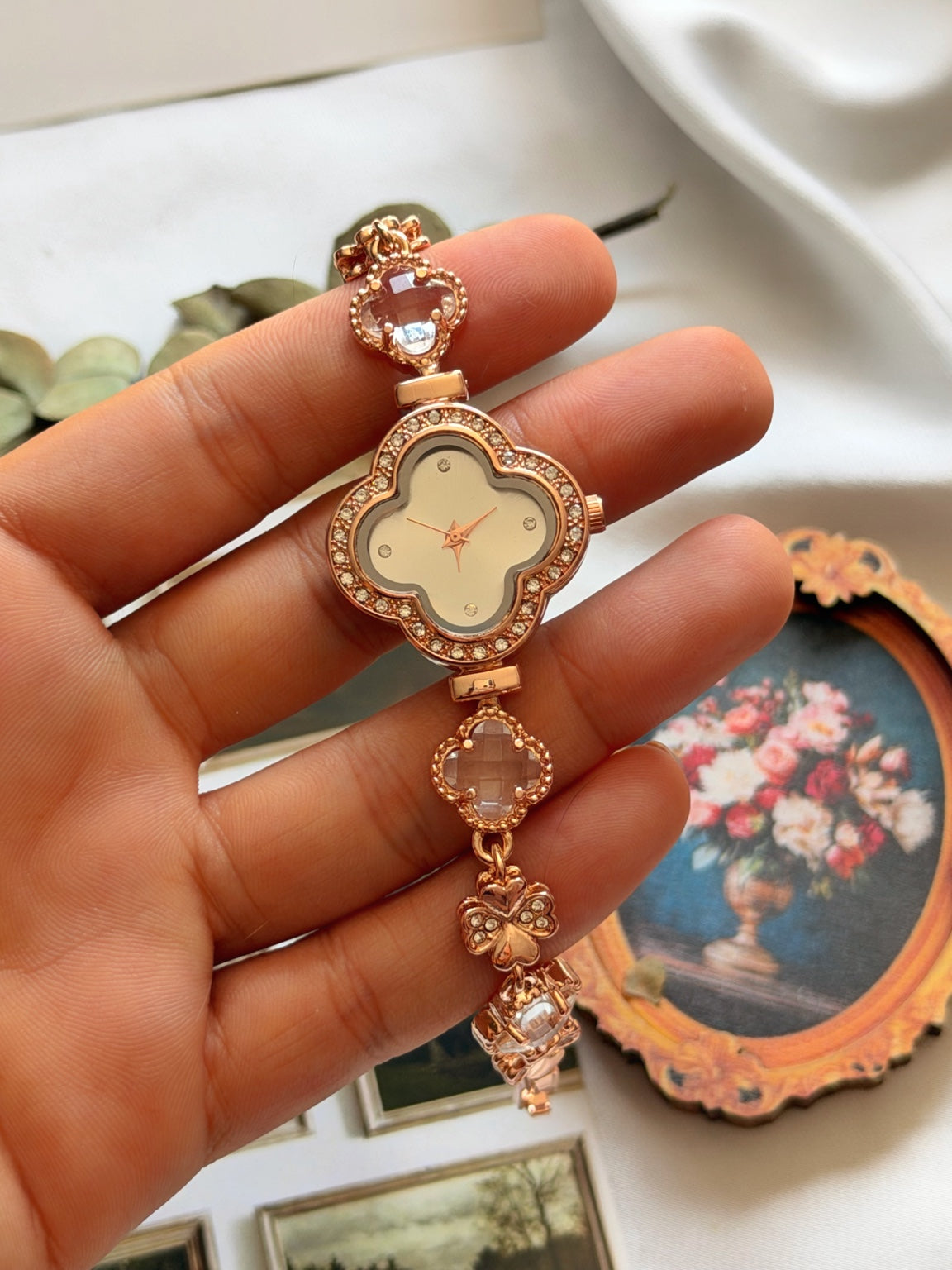 Rose gold kadın saatin yonca kadranı, şeffaf yonca taşları ve kelebek detaylı kordonunun elde görünümü