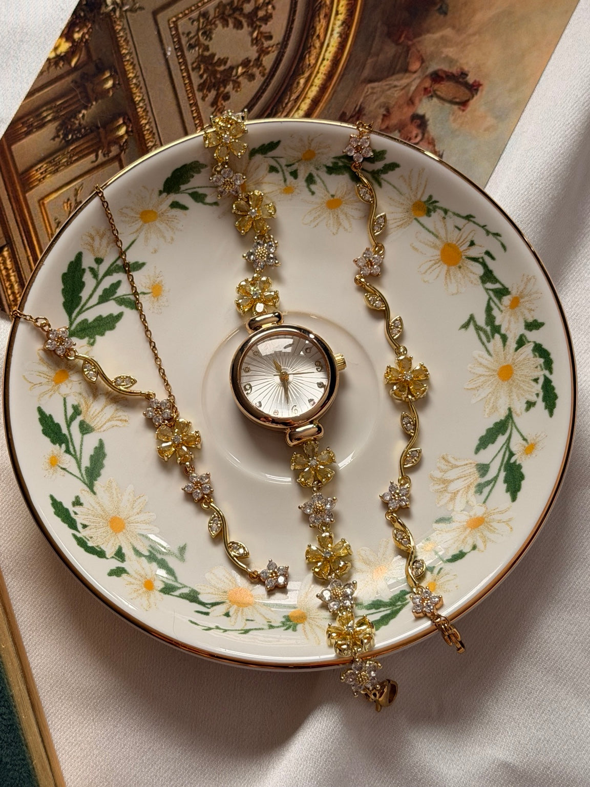 Sarı çiçekli gold saat, çelik kolye ve çelik bileklikten oluşan 3'lü kadın takı seti çiçek desenli tabakta