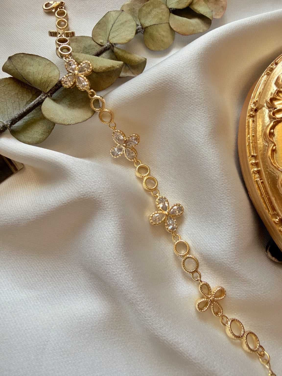 Gold tonlu şeffaf taşlı çiçekli kadın bilekliğin saten kumaş üzerinde uzun görünümü