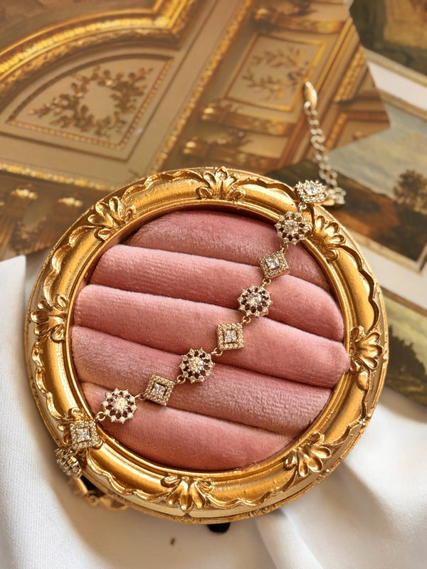Zirkon taşlı kare ve çiçek detaylı gold bilekliğin pembe kadife sunumda görünümü