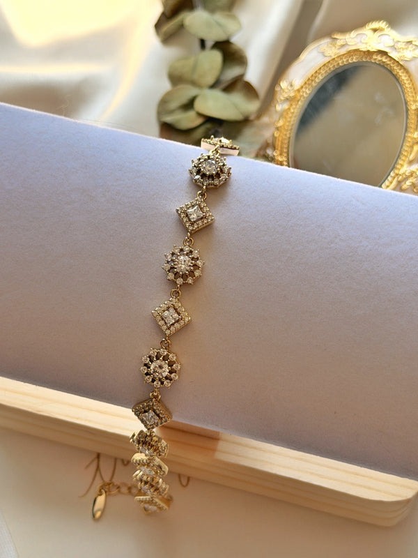 Taşlı kare ve çiçek motifli gold kadın bilekliğin beyaz stand üzerinde yakın görünümü